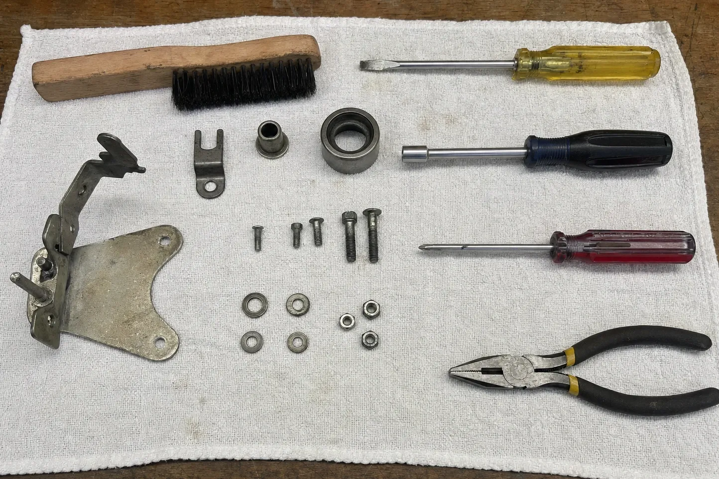 Hinge bracket, bushing, bearing race, bolts, washers and nuts arranged on a cloth with a wire brush, screwdrivers and pliers